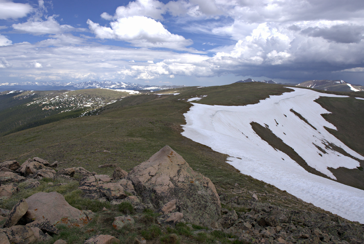 A dirt trail running down a mountainside. As the trail dips below the horizon, the sky above grows dark with clouds.